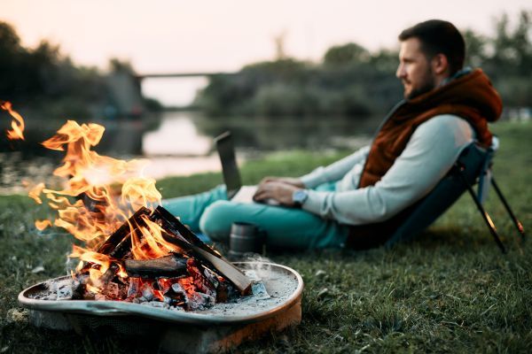 Man using his laptop outside near a campfire