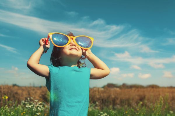 Little kid with big sunglasses smiling upwards towards the sun